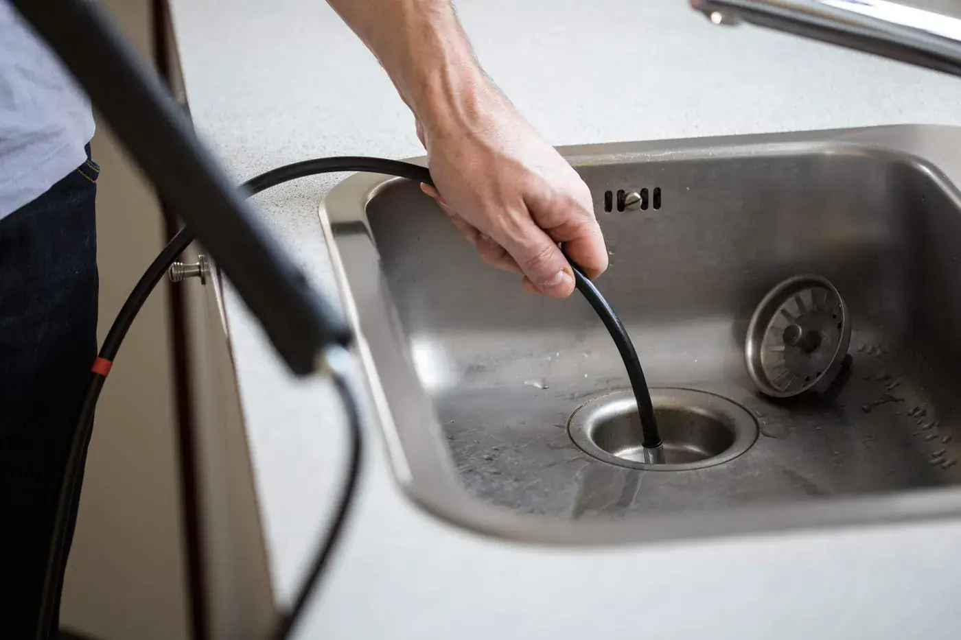 Installateur führt eine Reinigungsspirale in einen verstopften Küchenabfluss ein